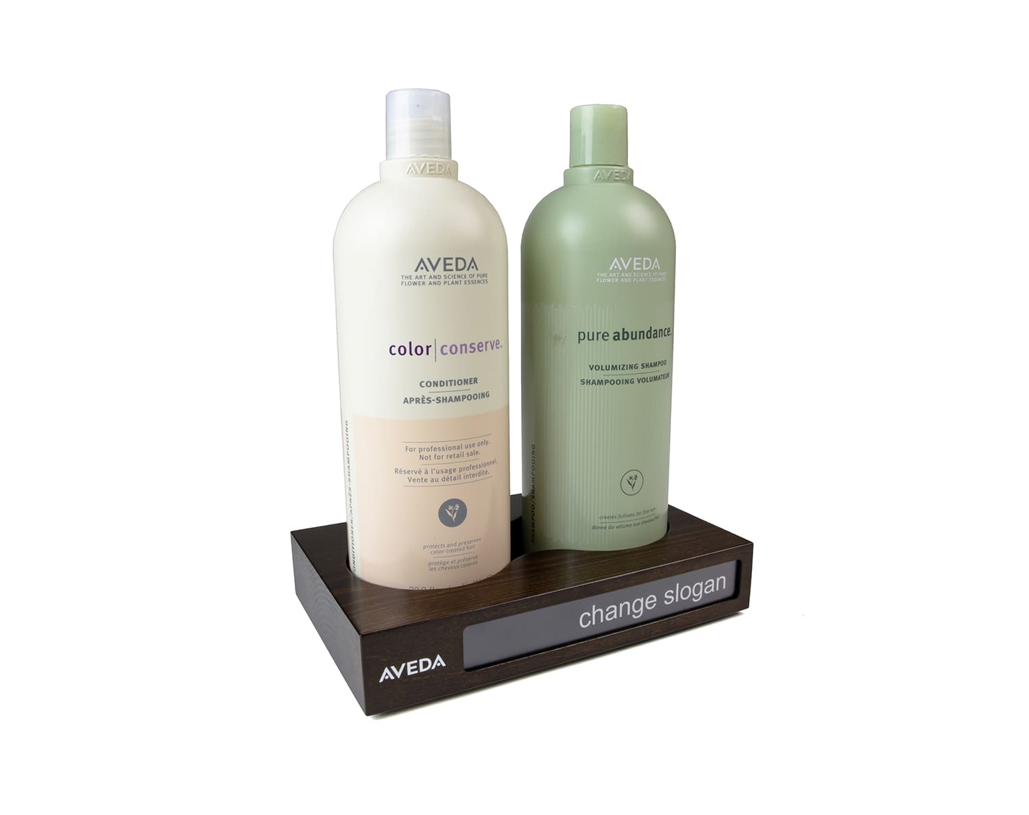 Dark stained wooden AVEDA POS block holding two bottles with a swap-in slogan panel on the front
